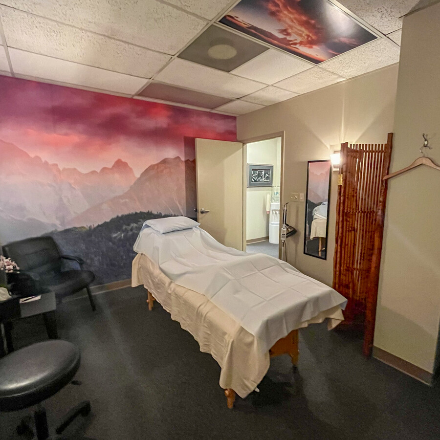 Metro Acupuncture's treatment room in Atlanta: massage table, pink sky mural, black chair, bamboo partition, sunset ceiling