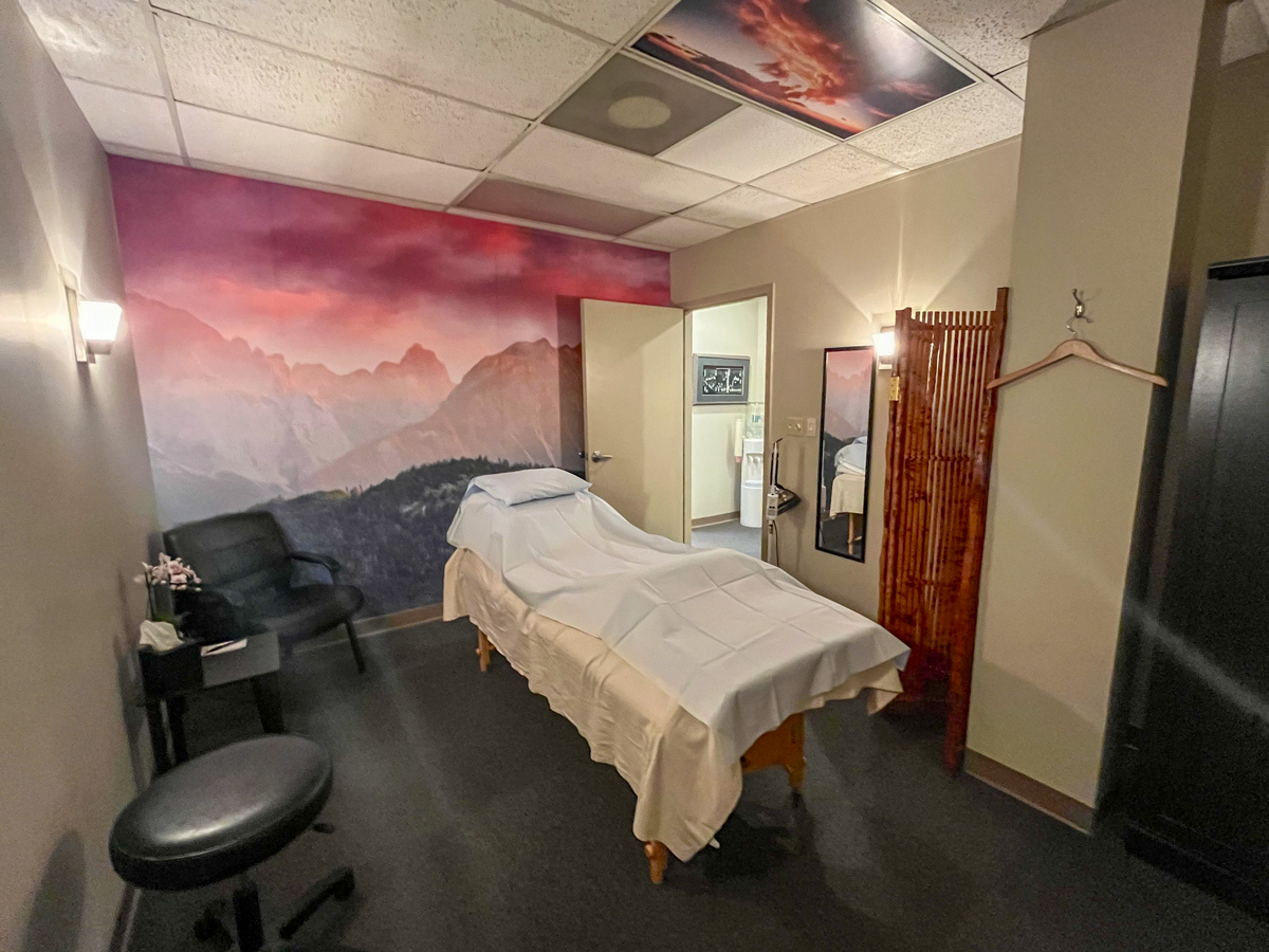 Metro Acupuncture's treatment room in Atlanta: massage table, pink sky mural, black chair, bamboo partition, sunset ceiling