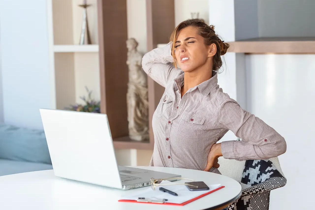 portrait-young-stressed-woman-sitting-home-office-desk-front-laptop-touching-aching-back-with-pained-expression-suffering-from-backache-after-working-laptop 1