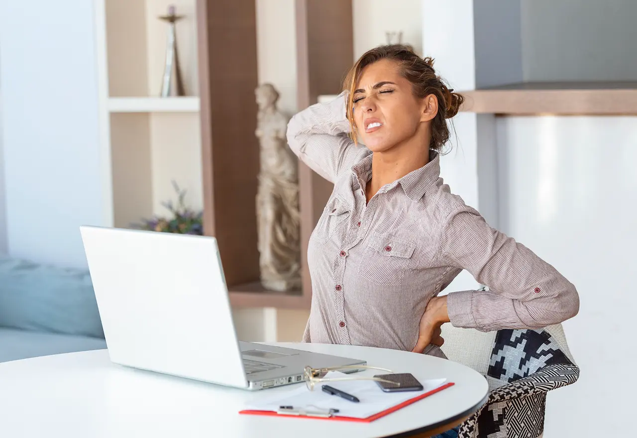 portrait-young-stressed-woman-sitting-home-office-desk-front-laptop-touching-aching-back-with-pained-expression-suffering-from-backache-after-working-laptop 1